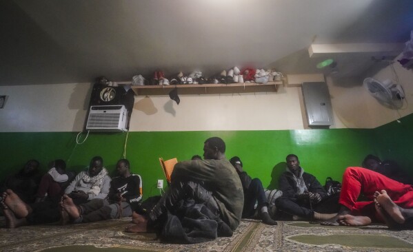 A Senegalese migrant, center, reads the Qurʾān following morning prayers, while other African migrants rest inside the main prayer area in the basement at Bronx's Masjid Ansaru-Deen mosque, Friday March 15, 2024, in New York. (AP Photo/Bebeto Matthews)